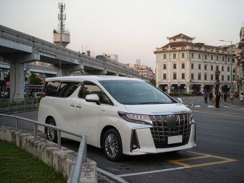 白色七座商务车停靠澳门街边上落客区，背景为轻轨高架